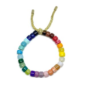 Puede incluir: Un brazalete de cuentas de colores arco&iacute;ris con cierre de cord&oacute;n dorado. Las cuentas est&aacute;n hechas de diferentes tipos de piedras preciosas y est&aacute;n dispuestas en un patr&oacute;n de arco&iacute;ris.