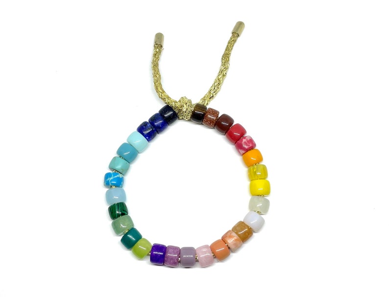 Puede incluir: Un brazalete de cuentas de colores arco&iacute;ris con cierre de cord&oacute;n dorado. Las cuentas est&aacute;n hechas de diferentes tipos de piedras preciosas y est&aacute;n dispuestas en un patr&oacute;n de arco&iacute;ris.