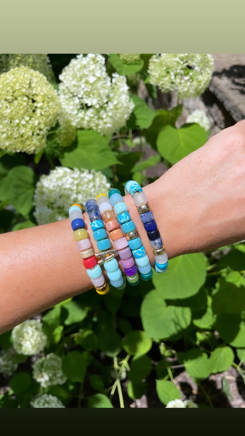 Puede incluir: Un conjunto de pulseras de cuentas de colores con una variedad de piedras y cuentas. Las pulseras est&aacute;n superpuestas en la mu&ntilde;eca de una persona y presentan cuentas turquesa, moradas, rosas, amarillas y azules.
