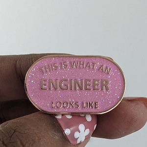 Könnte beinhalten: Rosa emaillierte Anstecknadel mit goldenen Glitzer und dem Text "This is what an engineer looks like".
