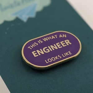 Könnte beinhalten: Violette und goldene Emaille-Anstecknadel mit dem Text "This is what an engineer looks like".