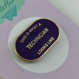 Pode incluir: Pin de esmalte roxo com acabamento dourado. O pin diz "É assim que um técnico parece".