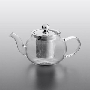 Könnte beinhalten: Eine klare Glas-Teekanne mit einem Deckel und einem Infuser aus Edelstahl. Die Teekanne hat einen gebogenen Ausguss und Griff. Der Infuser ist ein zylindrischer Netzkorb. Die Teekanne ist zum Aufbrühen von losem Tee konzipiert.