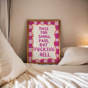 May include: A rectangular framed wall art piece featuring a white centre with a wavy orange border and pink and light pink vertical stripes. The text in pink reads: THIS TOO SHALL PASS, BUT FUCKING HELL. The frame is a simple, thin metallic gold colour.