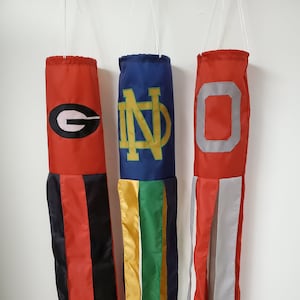 May include: Three red, blue, and white windsocks with team logos. The red windsock has a black and white 'G' logo, the blue windsock has a gold 'ND' logo, and the white windsock has a gray 'O' logo.