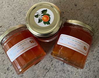 May include: Three glass jars of Seville Orange Marmalade with Sloe Gin. The jars have gold lids and labels with a white background and black text. The labels also feature a small orange and a sprig of orange blossoms.