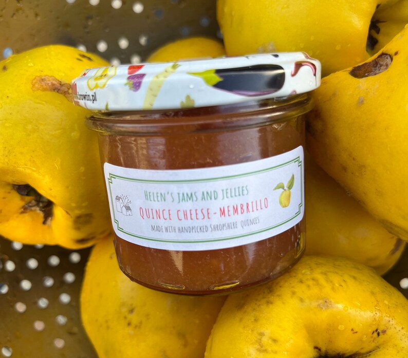 May include: A small glass jar of quince cheese, labeled "Helen's Jams and Jellies Quince Cheese - Membrillo Made with handpicked Shropshire quinces". The jar is surrounded by yellow quince fruit.