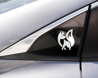 May include: A white vinyl decal of a stylized fox silhouette applied to the triangular rear side window of a silver car. The fox design features clean, bold lines depicting the animal in a seated position with its bushy tail curled upward.