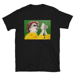 Könnte beinhalten: Ein schwarzes T-Shirt mit einer bunten Illustration einer Person, die in ein Mikrofon singt. Die Person trägt eine Sonnenbrille und eine gelbe Jacke. Der Hintergrund ist grün.