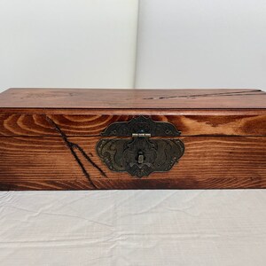 May include: A wooden box with a dark brown stain and a metal latch. The box has a rustic look with visible wood grain.