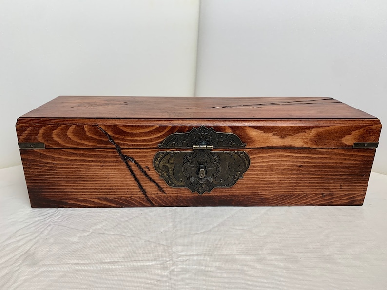 May include: A wooden box with a dark brown stain and a metal latch. The box has a rustic look with visible wood grain.