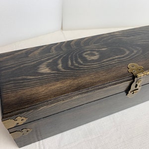 Pode incluir: Uma caixa de madeira escura com dobradi&ccedil;as e fechos de lat&atilde;o. A caixa tem um padr&atilde;o de gr&atilde;o de madeira natural e est&aacute; fechada.