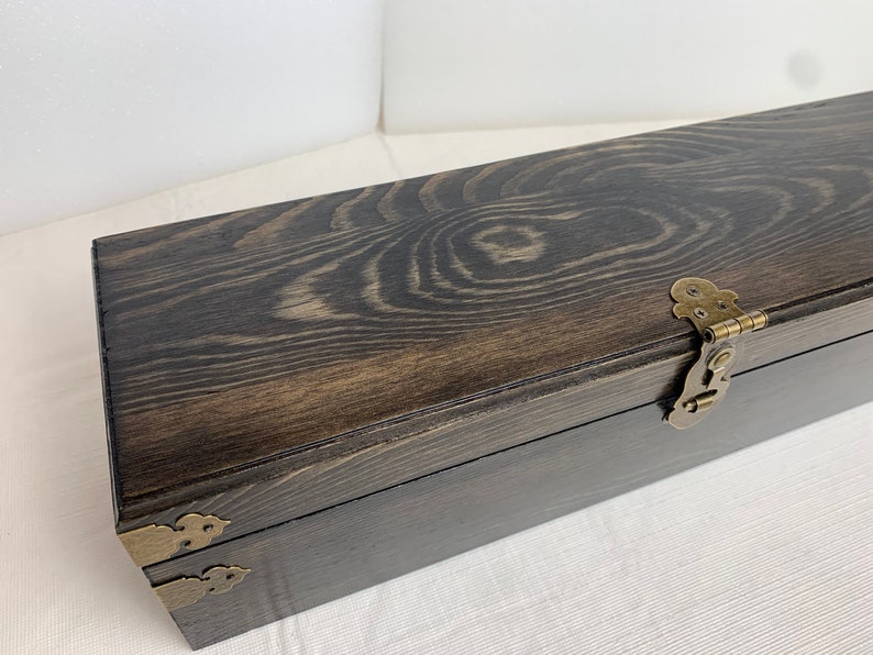 Pode incluir: Uma caixa de madeira escura com dobradi&ccedil;as e fechos de lat&atilde;o. A caixa tem um padr&atilde;o de gr&atilde;o de madeira natural e est&aacute; fechada.