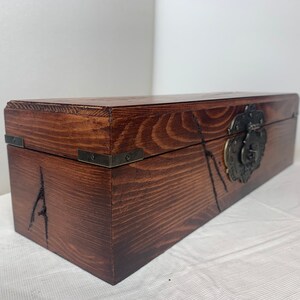 May include: A wooden box with a dark brown stain and a metal latch. The box has a carved design on the front and metal corner accents.