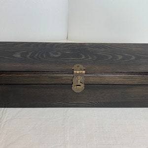 Pode incluir: Uma caixa de madeira escura com uma trava de lat&atilde;o e cantos decorativos. A caixa tem um padr&atilde;o de gr&atilde;o de madeira e est&aacute; fechada.