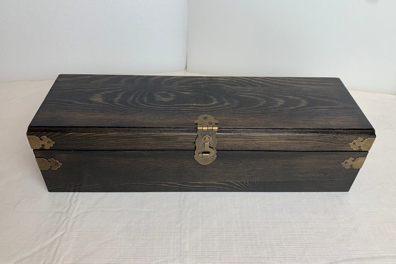 Pode incluir: Uma caixa de madeira escura com uma trava de lat&atilde;o e cantos decorativos. A caixa tem um padr&atilde;o de gr&atilde;o de madeira e est&aacute; fechada.