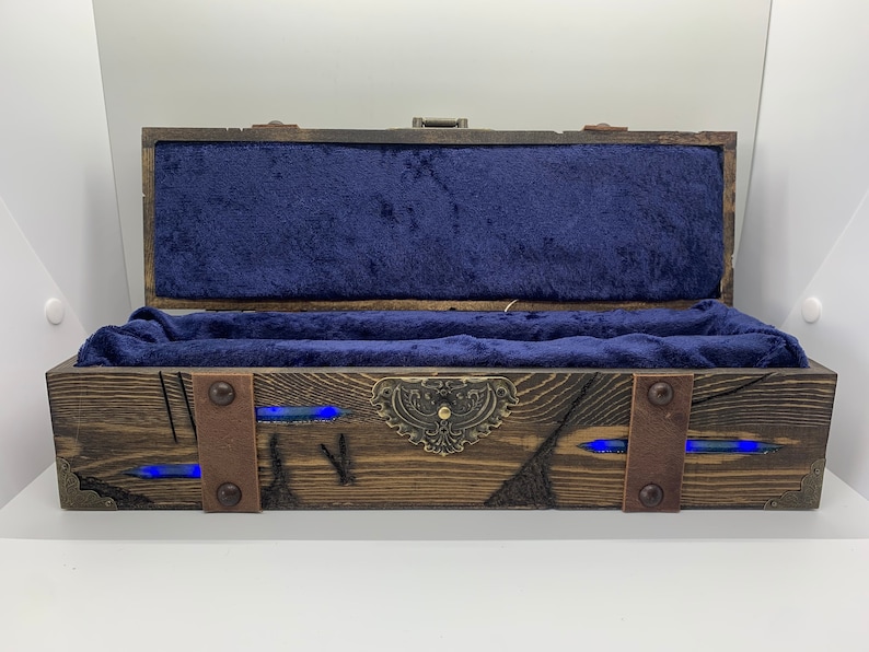 May include: A wooden box with a blue velvet interior and a metal latch. The box has a distressed wood finish and is decorated with metal accents. The box is lit from within with blue LED lights.