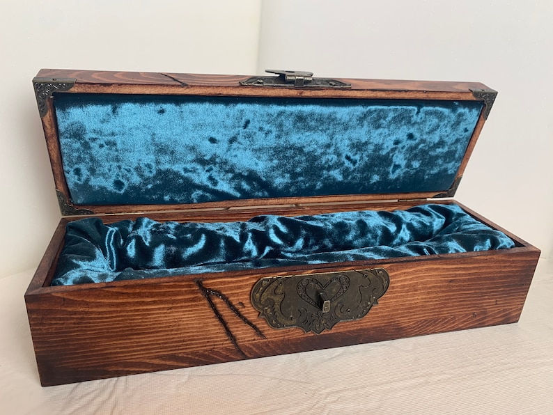 May include: A wooden box with a hinged lid and a blue velvet interior. The box has a decorative metal clasp with a heart design.