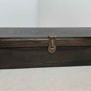 Pode incluir: Uma caixa de madeira castanho escuro com uma tampa articulada e detalhes em lat&atilde;o. A caixa tem uma trava de lat&atilde;o e pe&ccedil;as de canto decorativas.