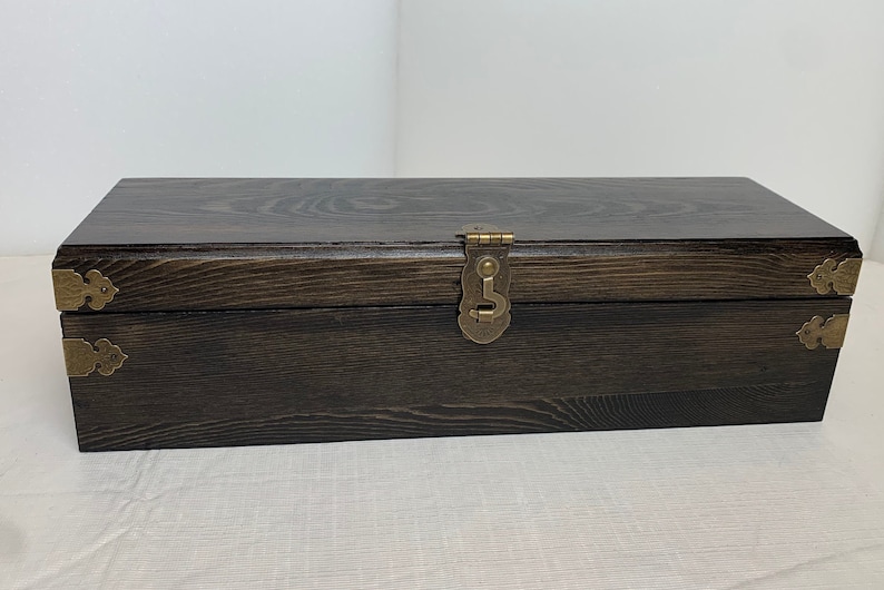 Pode incluir: Uma caixa de madeira castanho escuro com uma tampa articulada e detalhes em lat&atilde;o. A caixa tem uma trava de lat&atilde;o e pe&ccedil;as de canto decorativas.