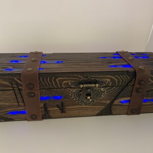 May include: A wooden box with a leather strap and metal accents. The box has a blue light inside and a metal latch.