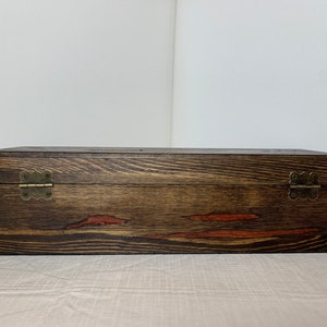 May include: A dark brown wooden box with two brass hinges. The box has a natural wood grain and a reddish-brown stain.