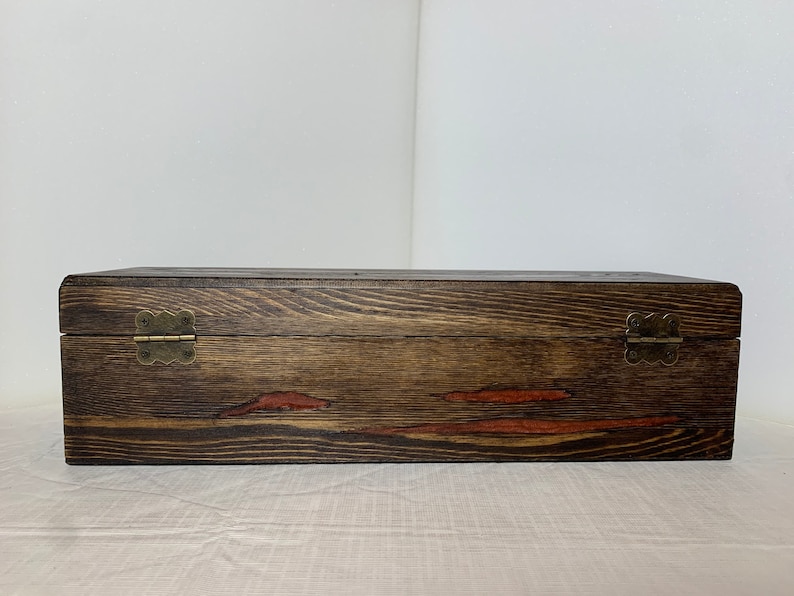 May include: A dark brown wooden box with two brass hinges. The box has a natural wood grain and a reddish-brown stain.