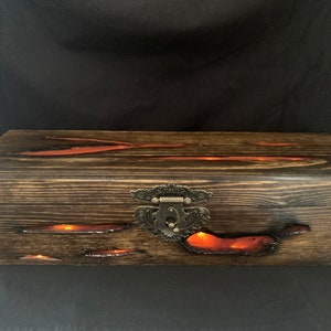 May include: A wooden box with a dark brown finish and a metal latch. The box has a red resin inlay that glows in the dark.