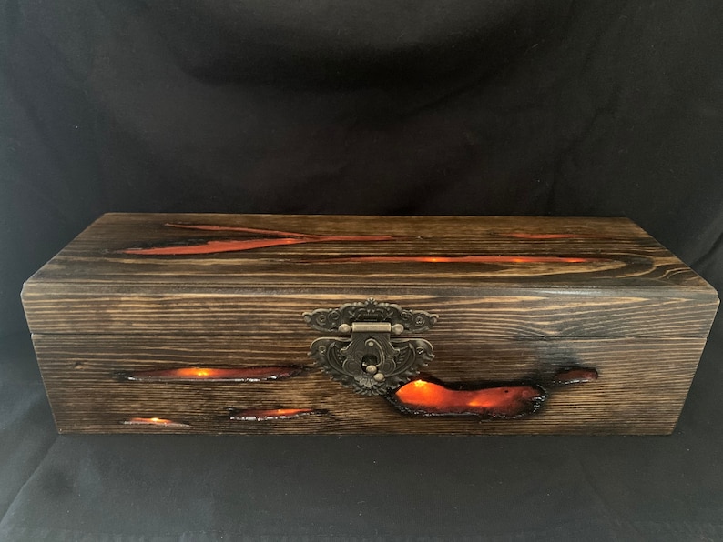 May include: A wooden box with a dark brown finish and a metal latch. The box has a red resin inlay that glows in the dark.