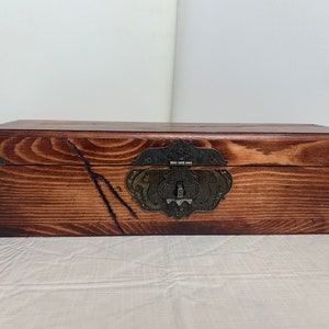 May include: A wooden box with a dark brown stain and a decorative metal latch. The box has a rustic look and is made of natural wood.
