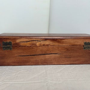 May include: A wooden box with a dark brown stain and brass hinges. The box has a rustic look with visible wood grain.