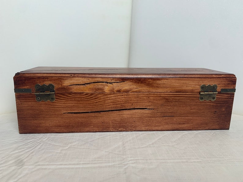 May include: A wooden box with a dark brown stain and brass hinges. The box has a rustic look with visible wood grain.