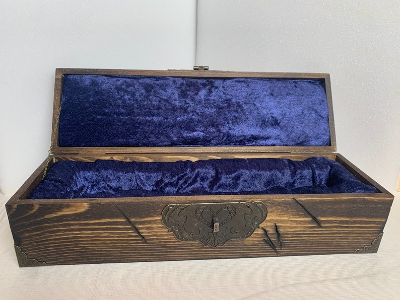 K&ouml;nnte beinhalten: Eine Holzkiste mit einer dunkelbraunen Beize und einer blauen Samtf&uuml;tterung. Die Kiste hat einen Metallverschluss und dekorative Metallakzente.