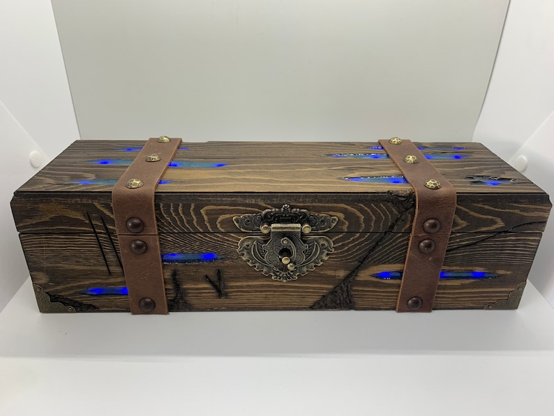 May include: A wooden box with a brown leather strap and metal accents. The box has a brass latch and blue LED lights inside.