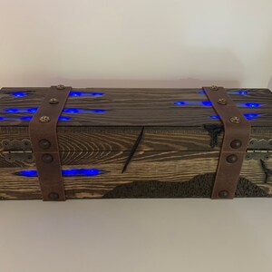 May include: A wooden box with a dark brown finish and leather straps. The box has a hinged lid and is decorated with blue LED lights.