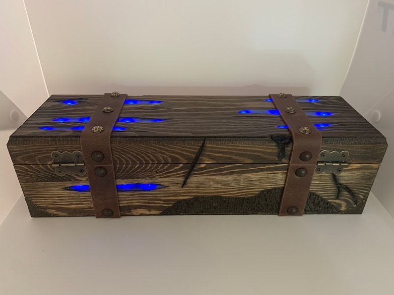 May include: A wooden box with a dark brown finish and leather straps. The box has a hinged lid and is decorated with blue LED lights.
