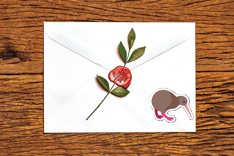 May include: A white envelope with a red wax seal and a brown kiwi bird sticker on a wooden surface.