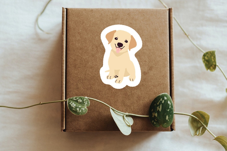 May include: A sticker of a yellow Labrador Retriever puppy sitting with its tongue sticking out. The puppy has brown eyes and black nose.