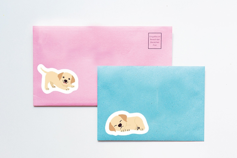 May include: Two envelopes, one pink and one blue, with stickers of a yellow Labrador puppy. The pink envelope has a sticker of the puppy standing and the blue envelope has a sticker of the puppy lying down.