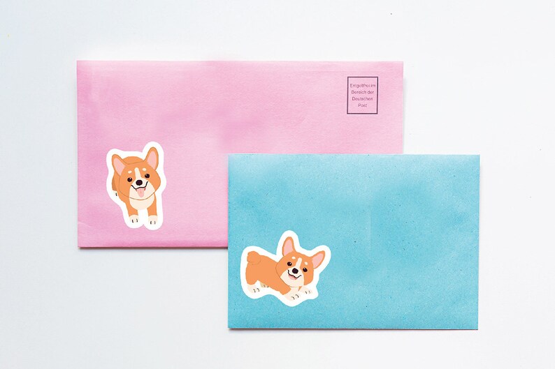 Puede incluir: Dos sobres, uno rosa y otro azul, con una imagen de dibujos animados de un perro corgi en cada uno. El sobre rosa tiene el texto "Entgeltmarken im Inland der Deutschen Post." impreso en &eacute;l.