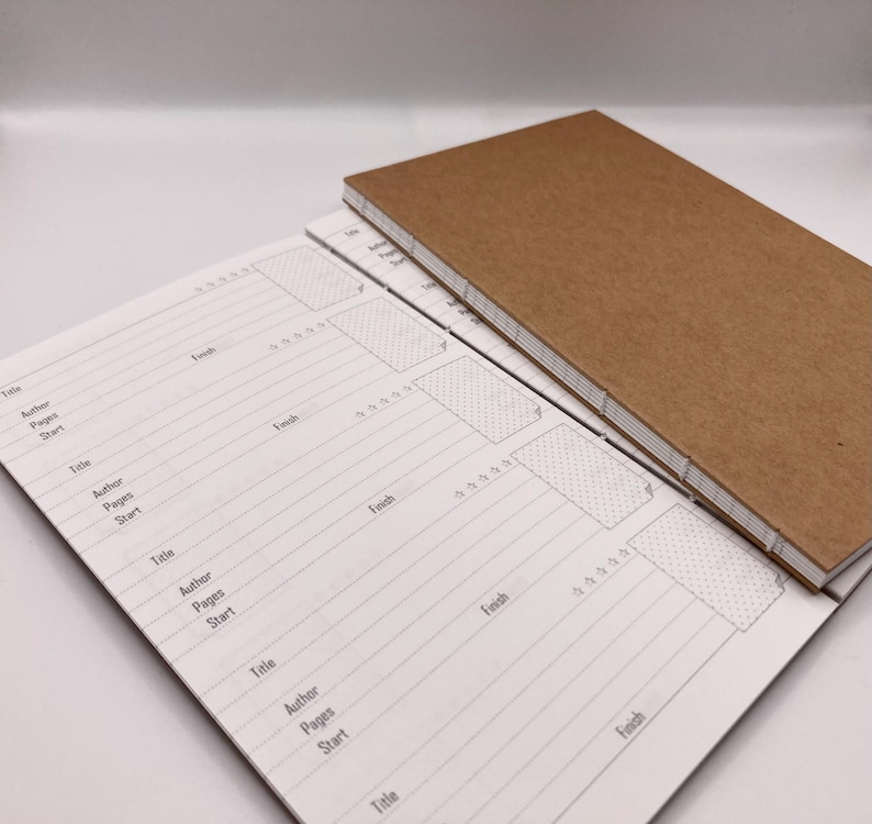 K&ouml;nnte beinhalten: Zwei handgefertigte Journale mit einem braunen Kraftpapier-Einband und einer gen&auml;hten Bindung. Die offenen Journalseiten haben ein liniertes Layout mit Feldern f&uuml;r Titel, Autor, Seiten und Start-/Enddaten. Die Journale sind zum Schreiben.