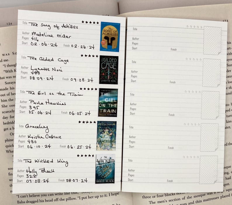 K&ouml;nnte beinhalten: Offenes Buch mit einem Lesetagebuch. Eintr&auml;ge umfassen Buchtitel wie "The Song of Achilles" und "The Gilded Cage" mit Autorennamen, Seitenzahlen und Daten. Kleine Buchcover-Bilder sind enthalten.