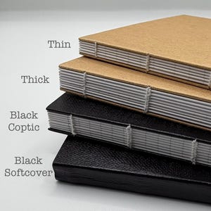 K&ouml;nnte beinhalten: Ein Stapel handgefertigter Notizb&uuml;cher mit sichtbaren N&auml;hten. Die oberen beiden Notizb&uuml;cher haben braune Umschl&auml;ge, beschriftet mit "Thin" und "Thick". Die unteren beiden Notizb&uuml;cher sind schwarz, beschriftet mit "Black Coptic" und "Black Softcover".
