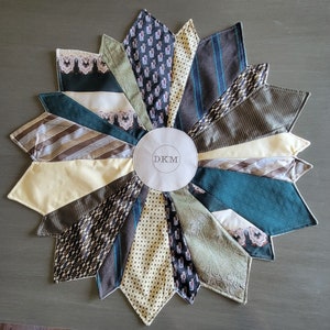 May include: A circular, multi-colored, fabric wall hanging with a white center circle that says "DKM". The fabric is made of different patterns of ties.