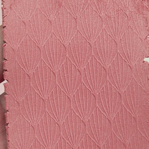 May include: A close-up of a pink textured surface with a repeating geometric pattern of overlapping arches. The surface has a subtle shimmer.