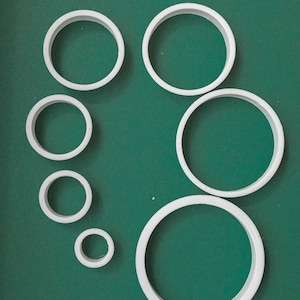 Op de afbeelding: Een set van zeven witte ronde koekjesvormen van plastic in verschillende maten op een groene ondergrond.