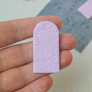 May include: A light pink, floral patterned, arch-shaped clay piece.