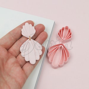 Może przedstawiać: Różowe kolczyki z muszli z polimerowej gliny z złotym akcentem. Na zdjęciu widoczne są również trzy wykrawacze do ciasteczek w kształcie muszli.