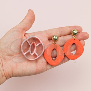 Könnte beinhalten: Ein Paar orangefarbene Ohrringe mit goldener Verzierung und einer rosa Plastikform zum Herstellen der Ohrringe.