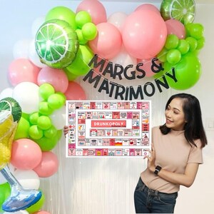 May include: A pink and green balloon arch with the text "MARGS & MATRIMONY" in black letters. A person is holding a game board with the text "DRUNKOPOLY" in red letters.